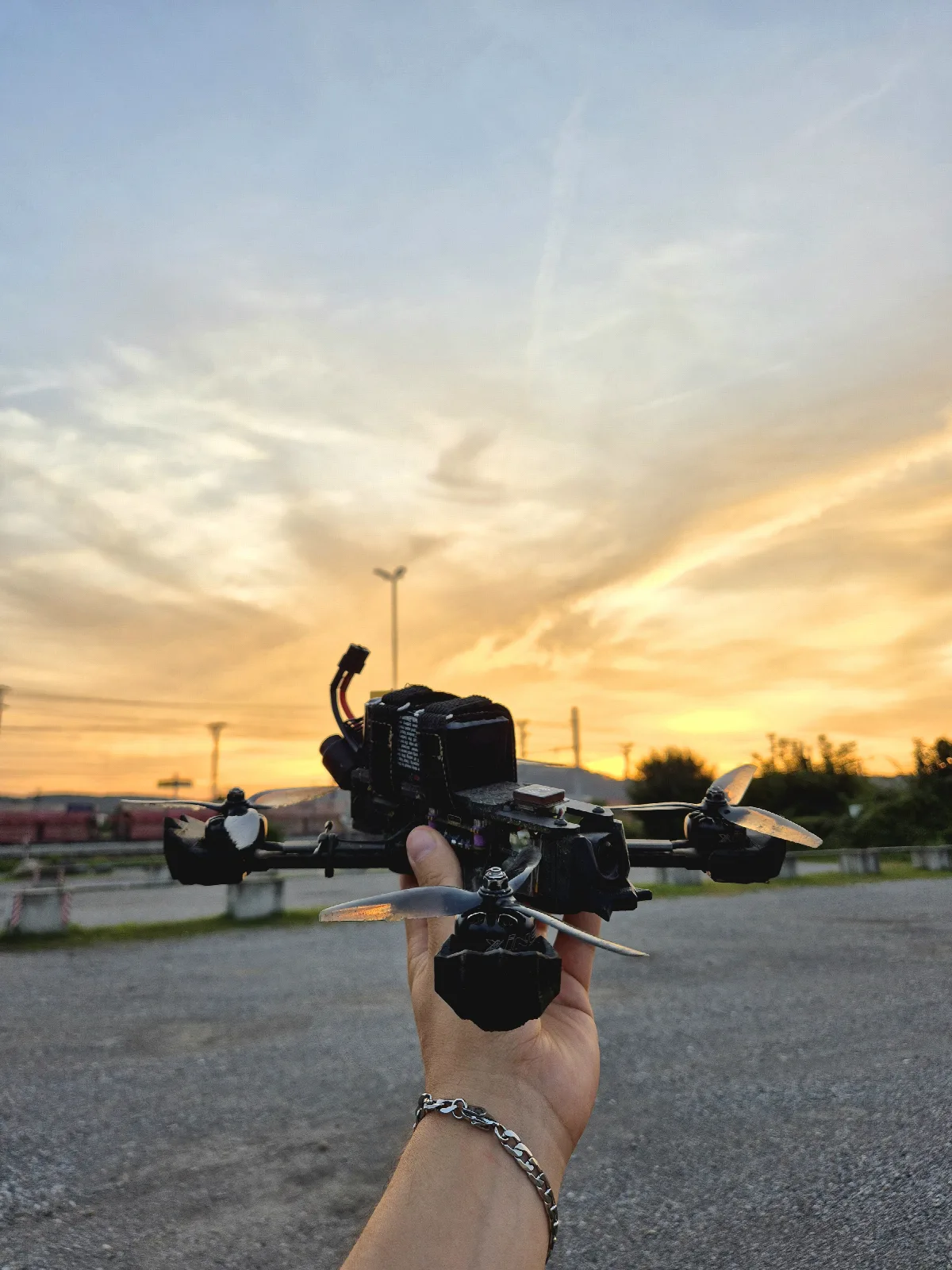 Selbst gebaute FPV-Freestyle-Drohne in der Hand, dahinter Sonnenuntergang