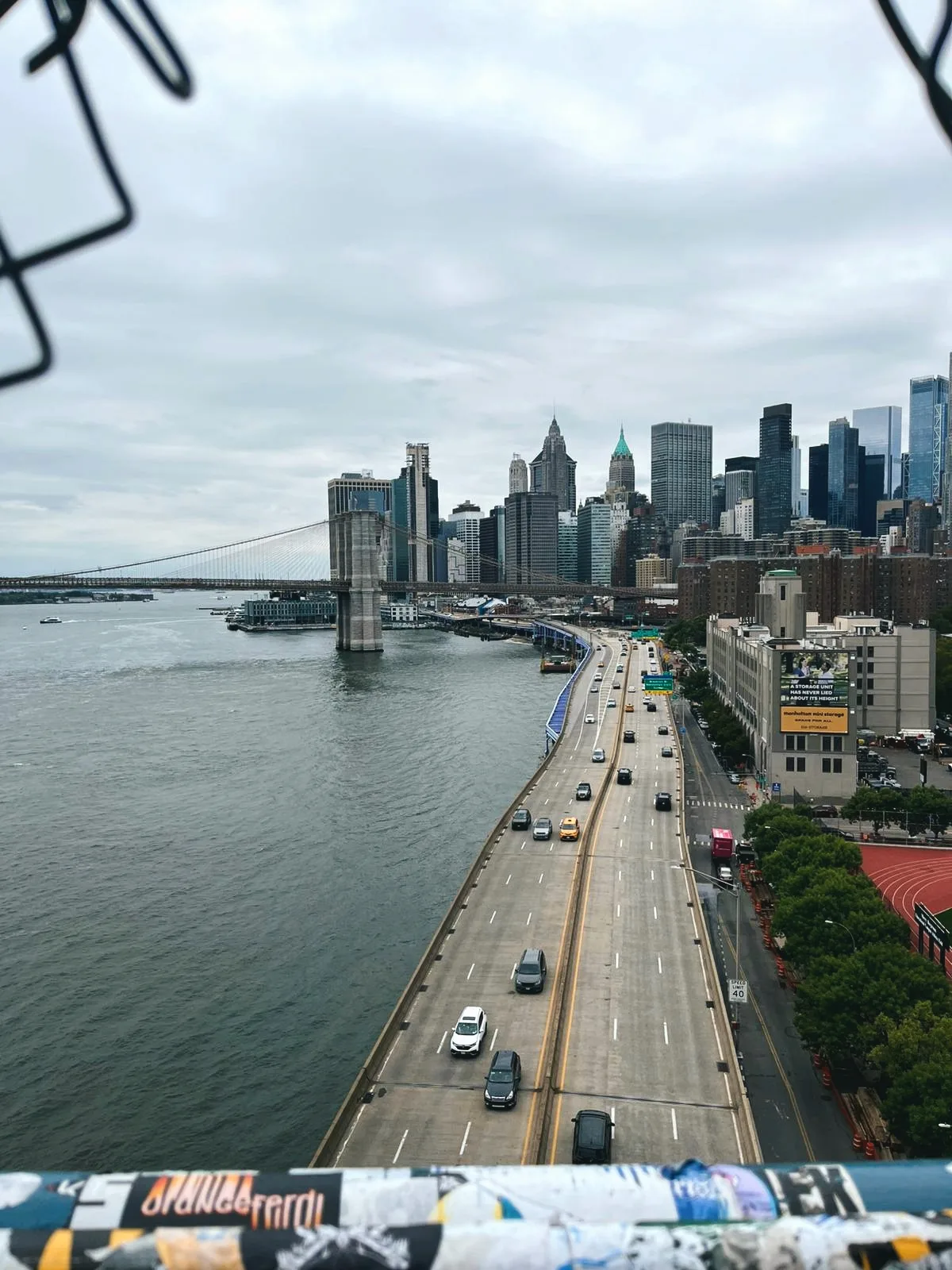 orangeferdi-Sticker am Geländer der Manhattan Bridge, dahinter die Brooklyn Bridge und Lower Manhattan