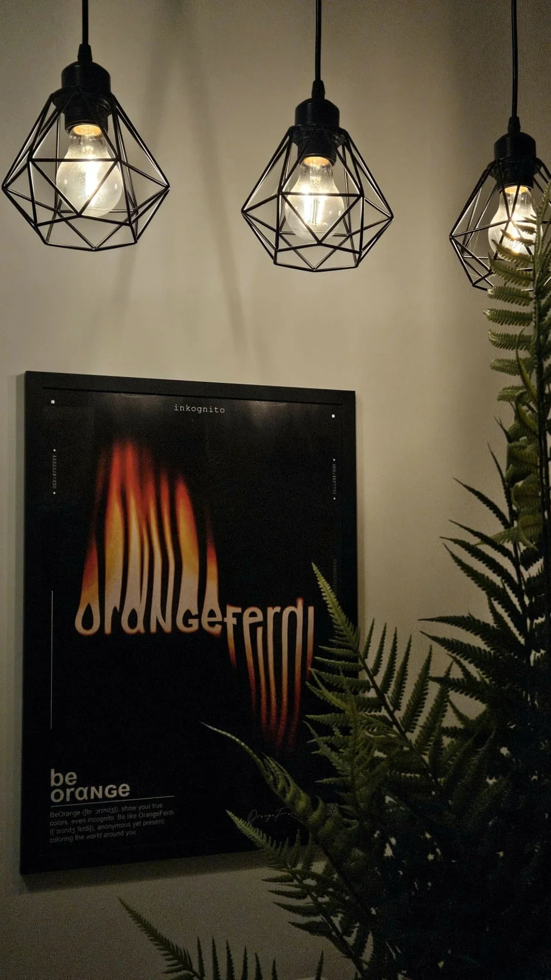Gerahmtes orangeferdi-Poster in A2 an der Wand, darüber drei Käfiglampen